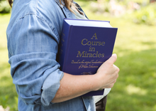 Load image into Gallery viewer, A person holding the large purple hardcover edition of A Course in Miracles Complete and Annotated Edition to show size and scale.